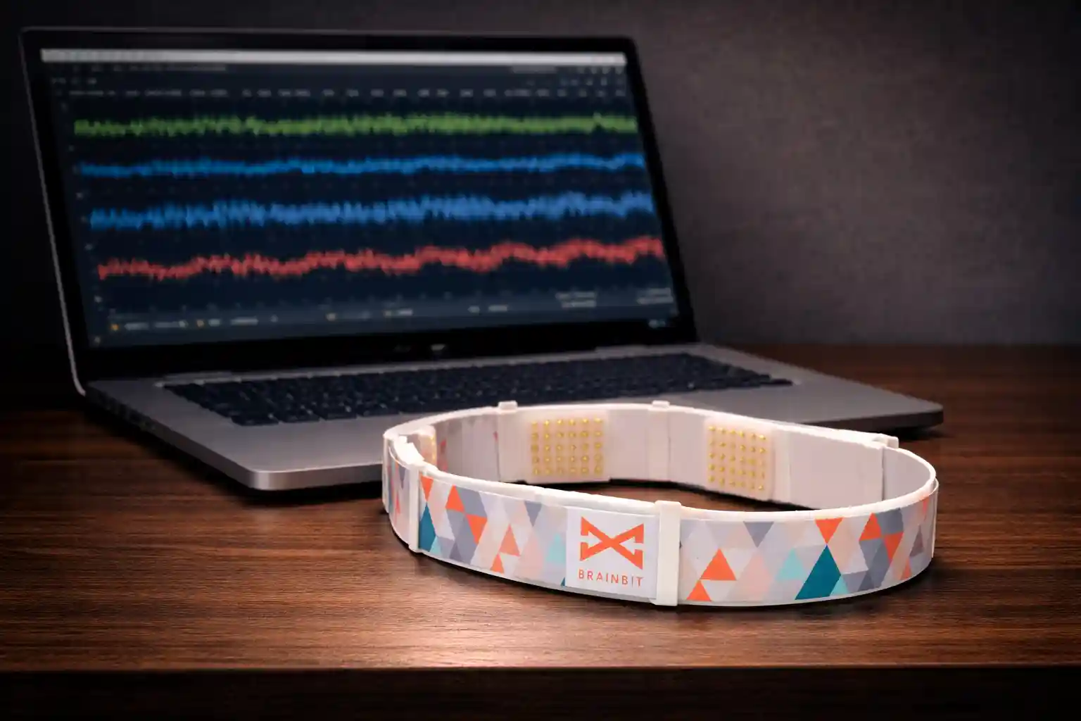 BrainBit EEG headset on a desk beside a laptop showing waveform data